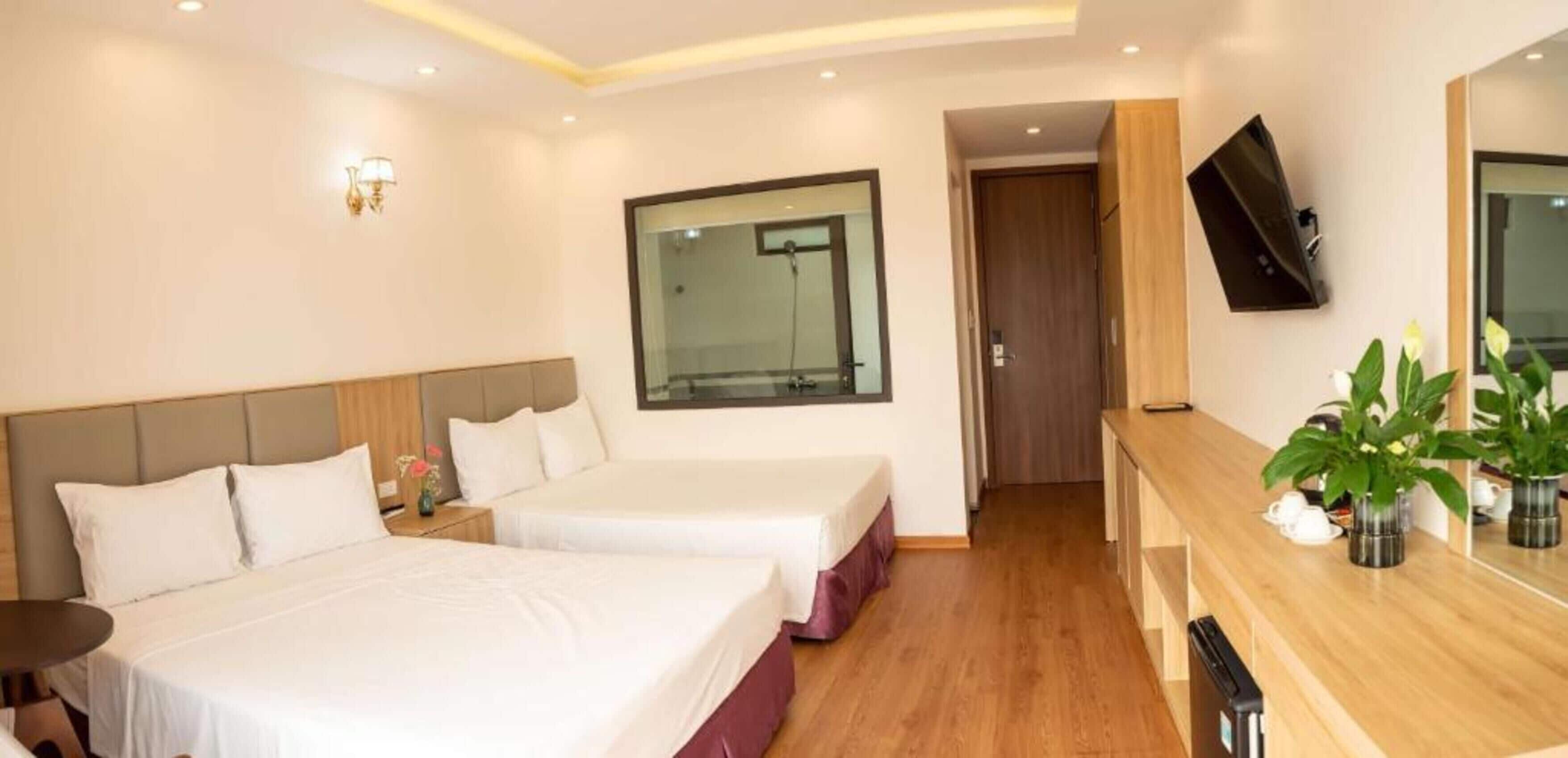 A hotel room with two beds, a wooden desk, a TV, and a large window.
