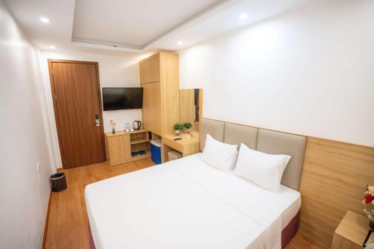 Une chambre d’hôtel avec un grand lit, une armoire en bois, un bureau avec une chaise, une télévision et une petite plante.