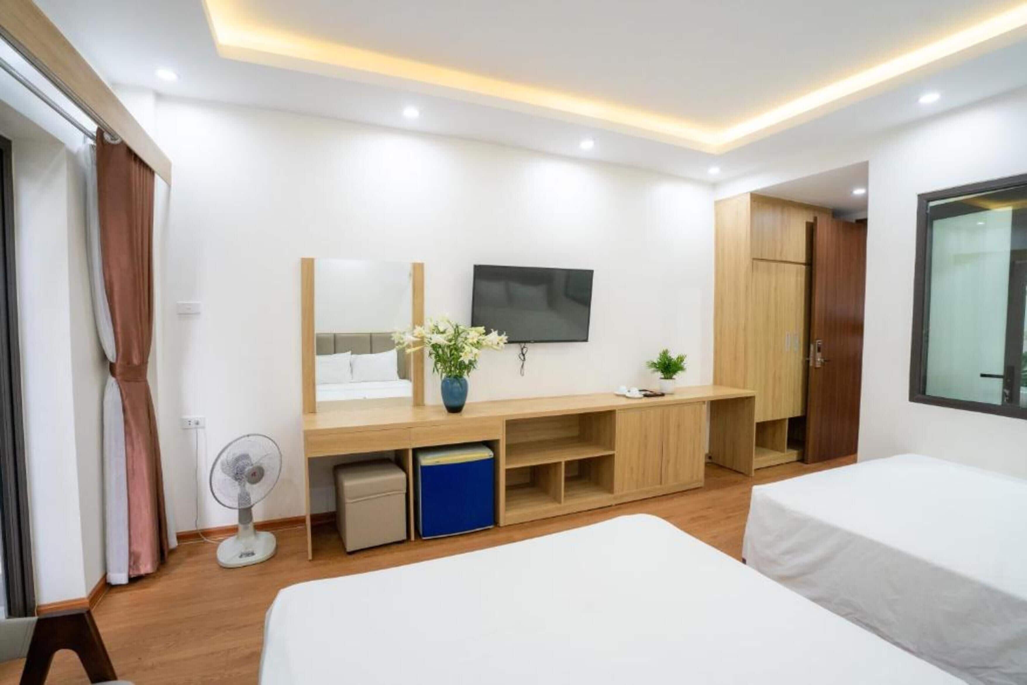 Una habitación de hotel moderna con una cama grande, un televisor, un escritorio con computadora, un ventilador pequeño y un armario.