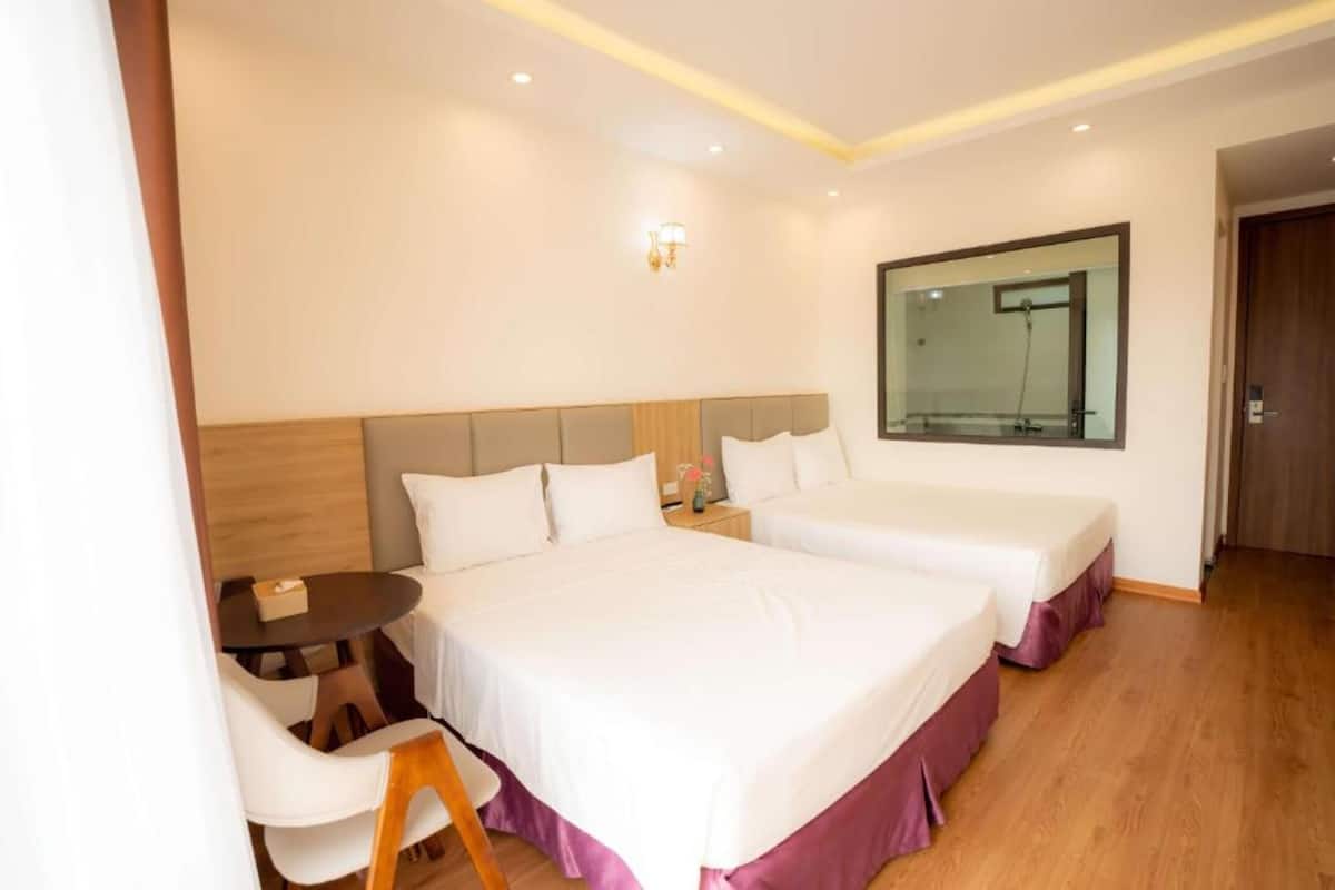 Une chambre d’hôtel avec deux lits, une petite table avec des chaises et un grand miroir au mur.