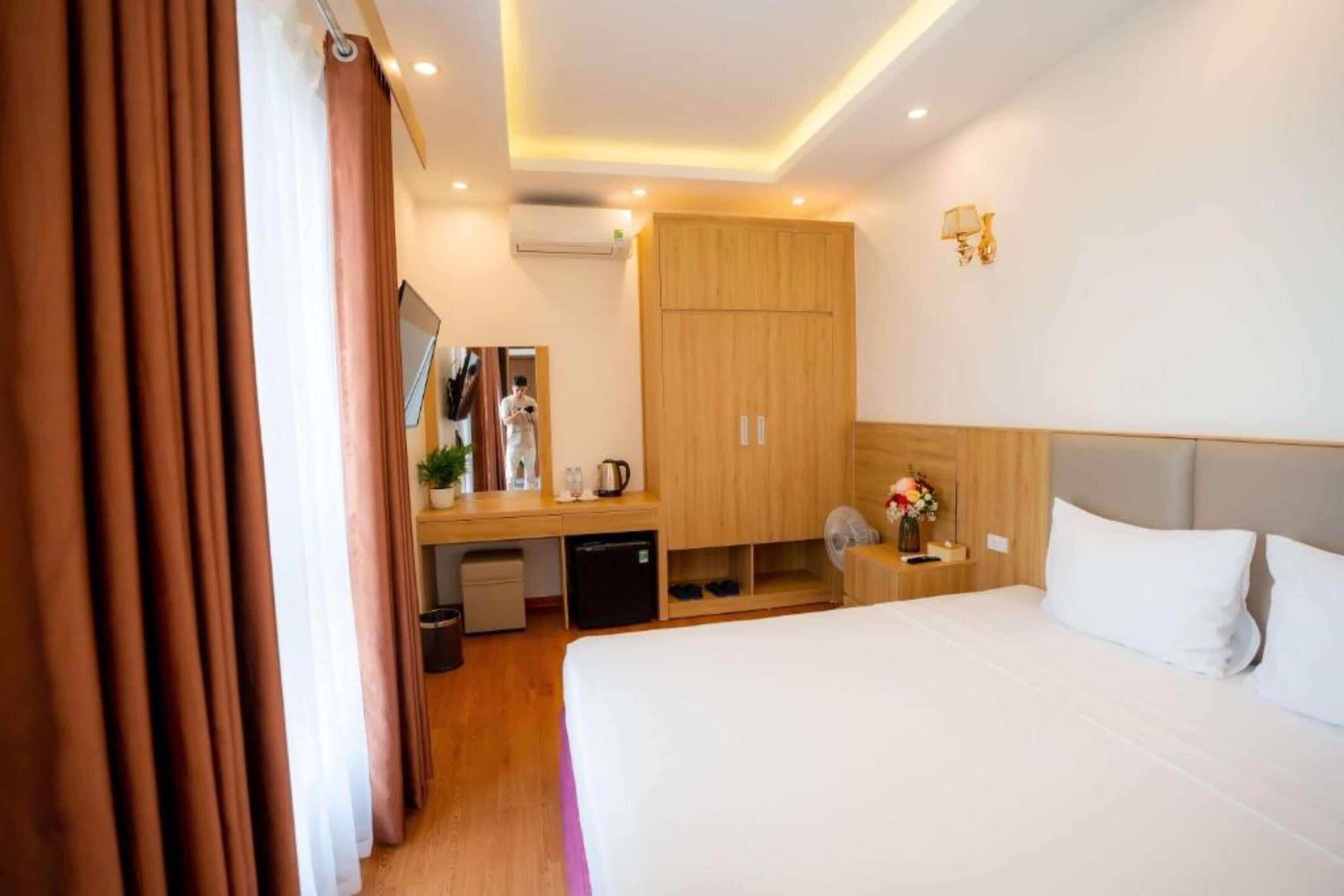 A hotel room with a bed, a desk, a wardrobe, a mirror, and a small kitchenette.