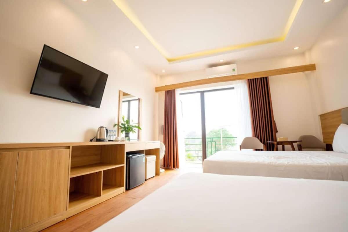 Une chambre d’hôtel comprenant un lit, un bureau avec un ordinateur, un téléviseur fixé au mur et un balcon avec des rideaux.