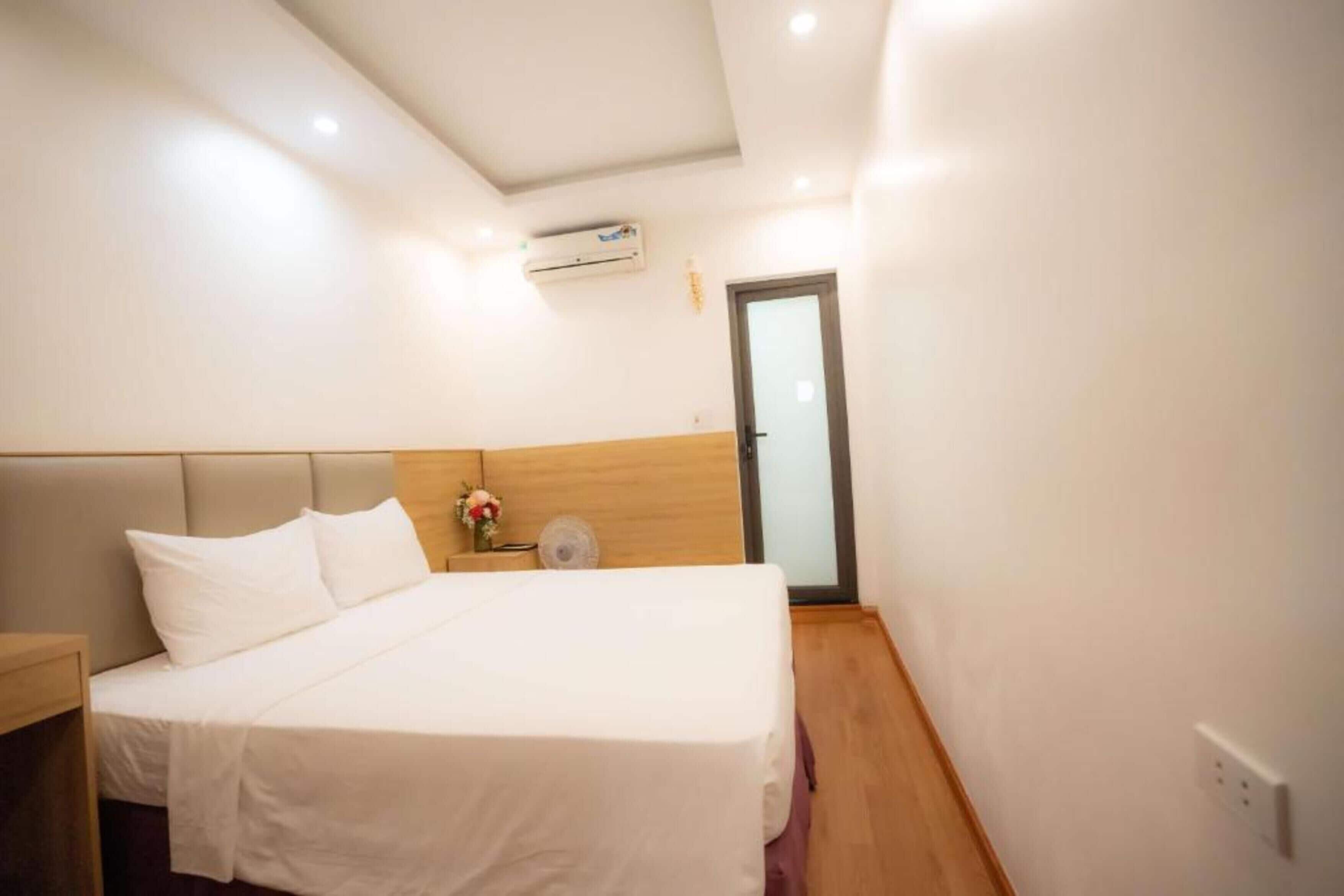 A hotel room with a bed, a nightstand, a wall-mounted air conditioner, and a door.