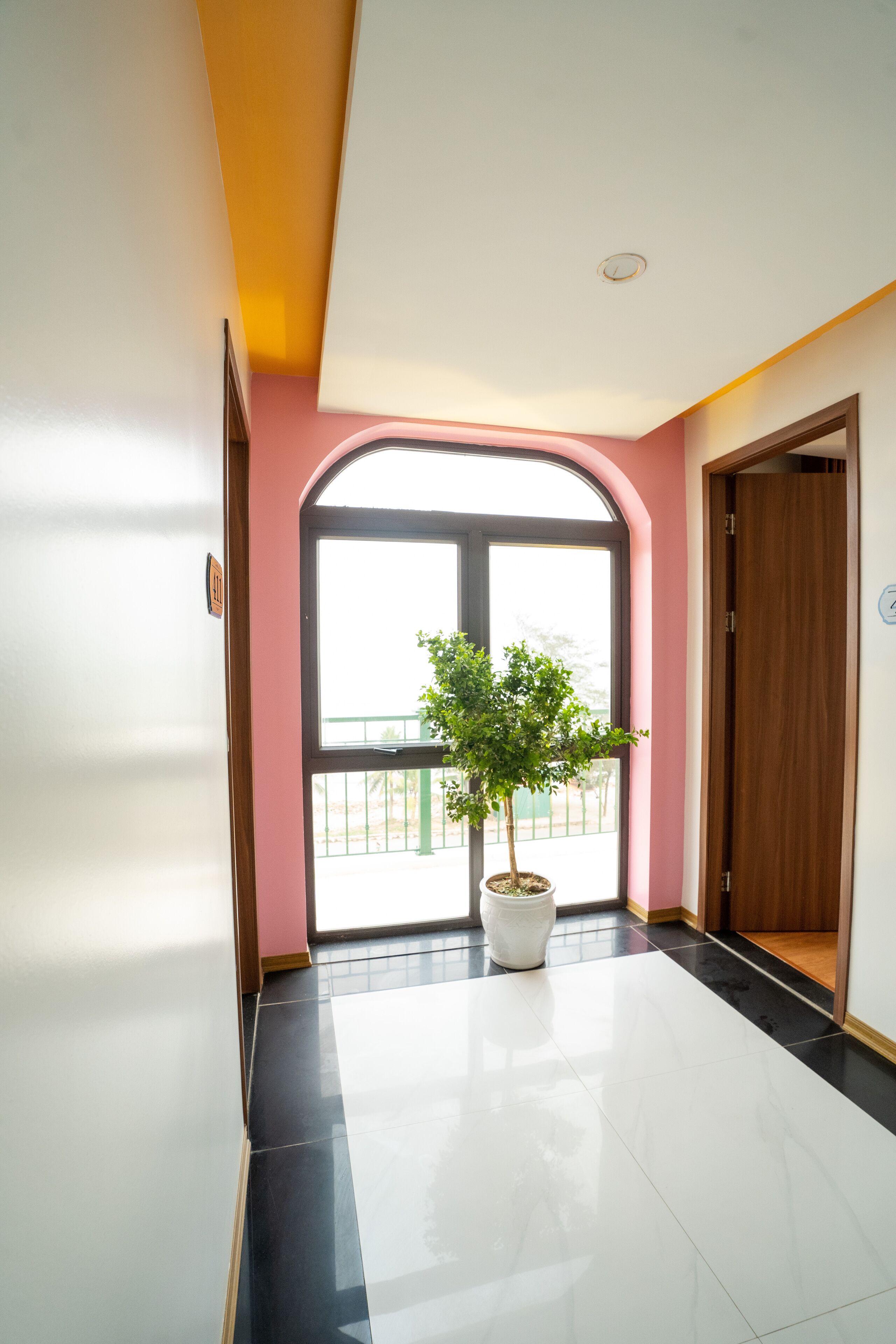 A hallway with a potted plant, a large arched window, and a wooden door.