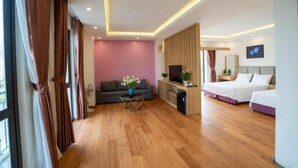 Una habitación de hotel moderna con piso de madera, un sofá, un escritorio con televisor y dos camas.