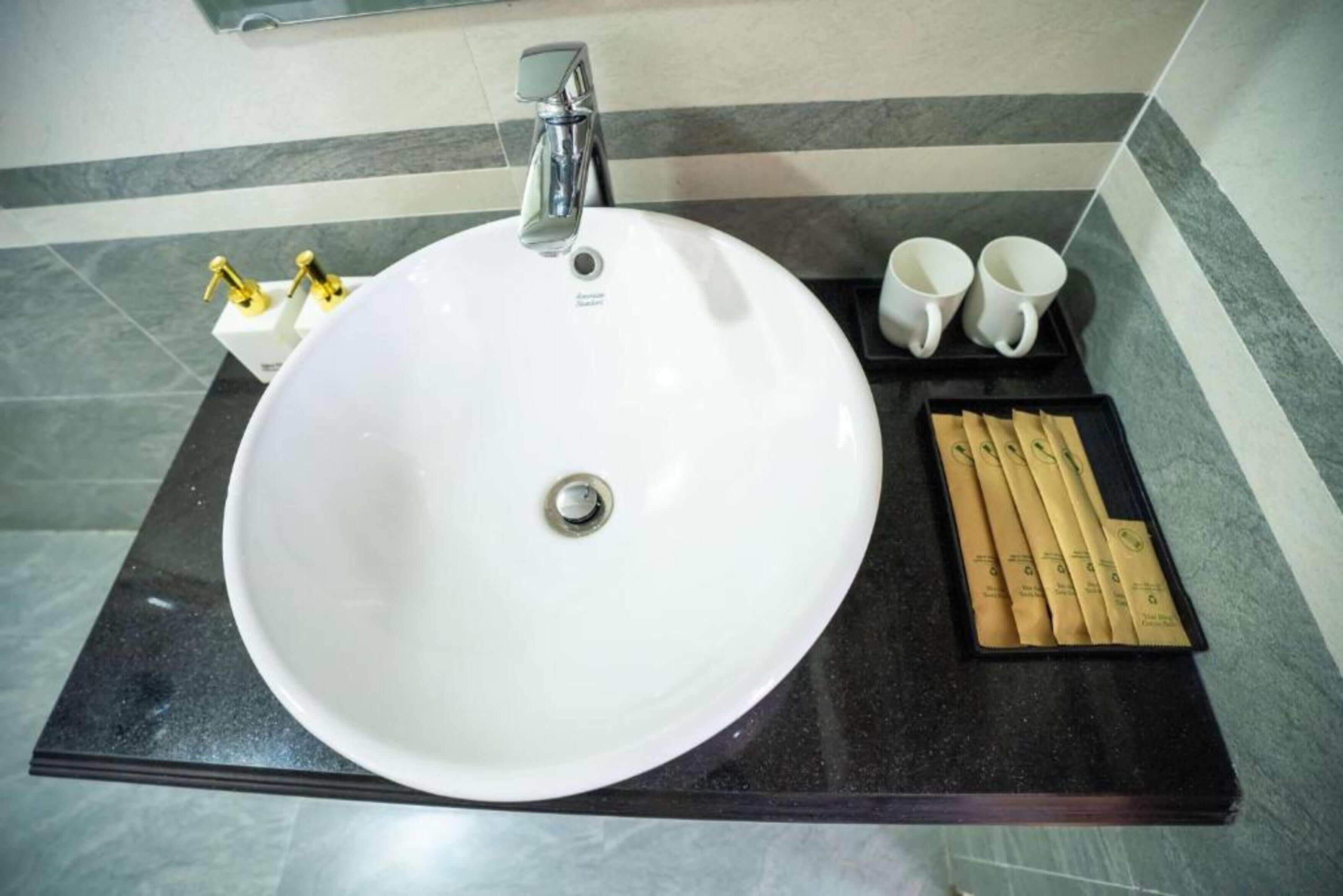 Un baño con un lavabo blanco, un espejo, dos grifos dorados y una bandeja con toallas y un cepillo de dientes.