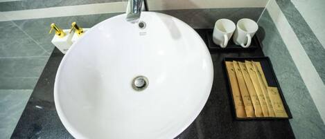 Un baño con un lavabo blanco, un espejo, dos grifos dorados y una bandeja con toallas y un cepillo de dientes.