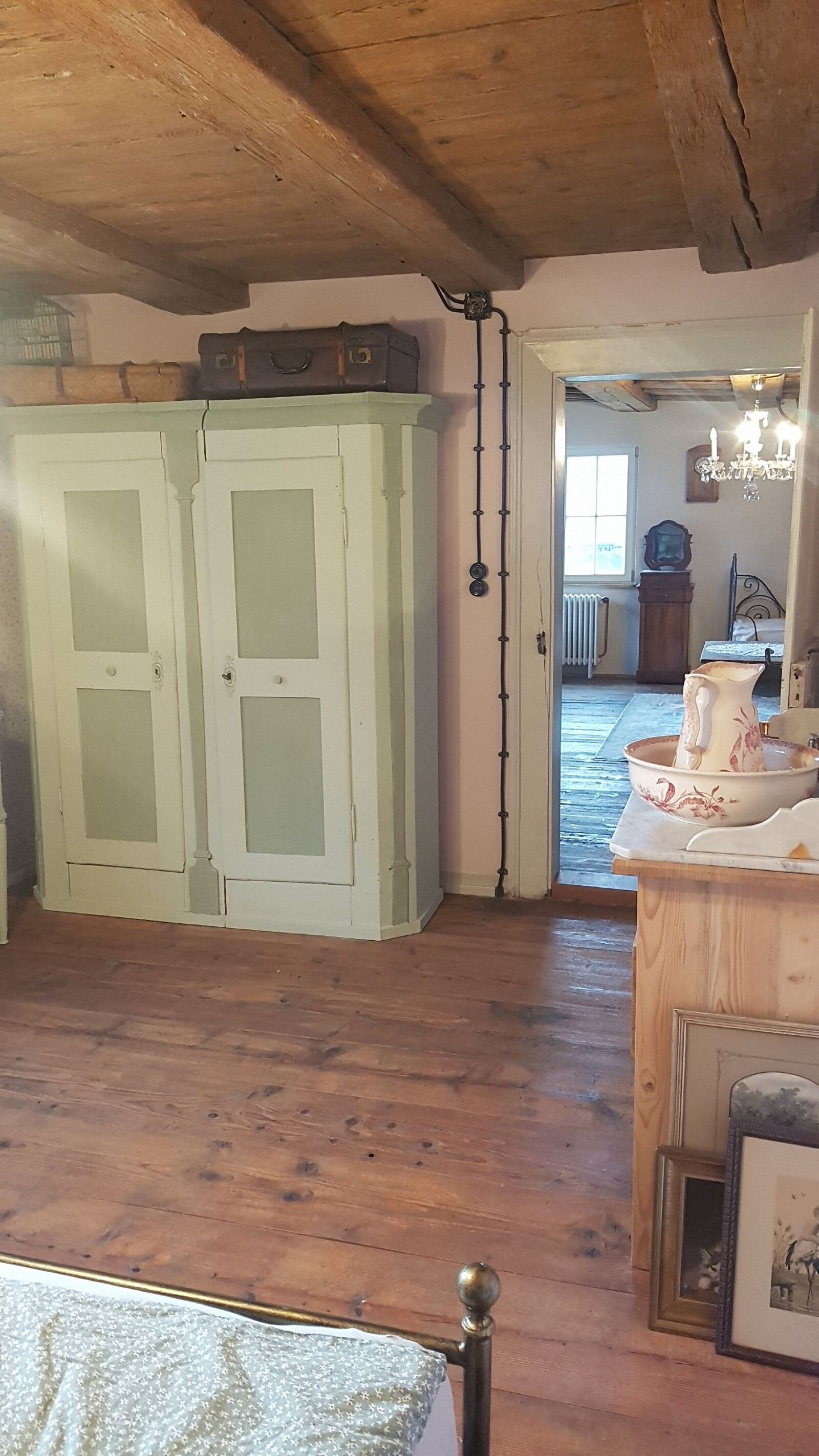 A room with wooden floors, a bed with a metal frame, a white cabinet with glass doors, and a chandelier.