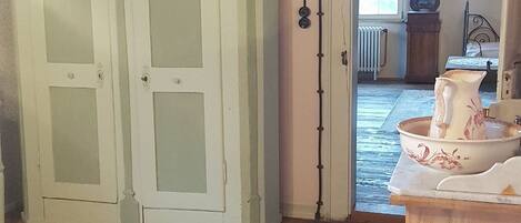 A room with wooden floors, a bed with a metal frame, a white cabinet with glass doors, and a chandelier.