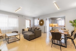 A modern living room with a sectional sofa, a dining table with chairs, and a kitchen area in the background.