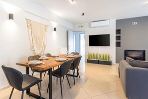 Un salon moderne comprenant un coin repas, un téléviseur à écran plat fixé au mur et un canapé gris.