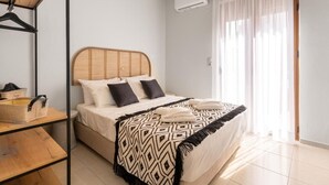 A bedroom with a bed, a hanging light fixture, a window with curtains, and a wooden floor.
