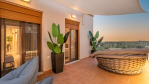 A balcony with a cushioned seating area, large potted plants, and a view of the landscape.