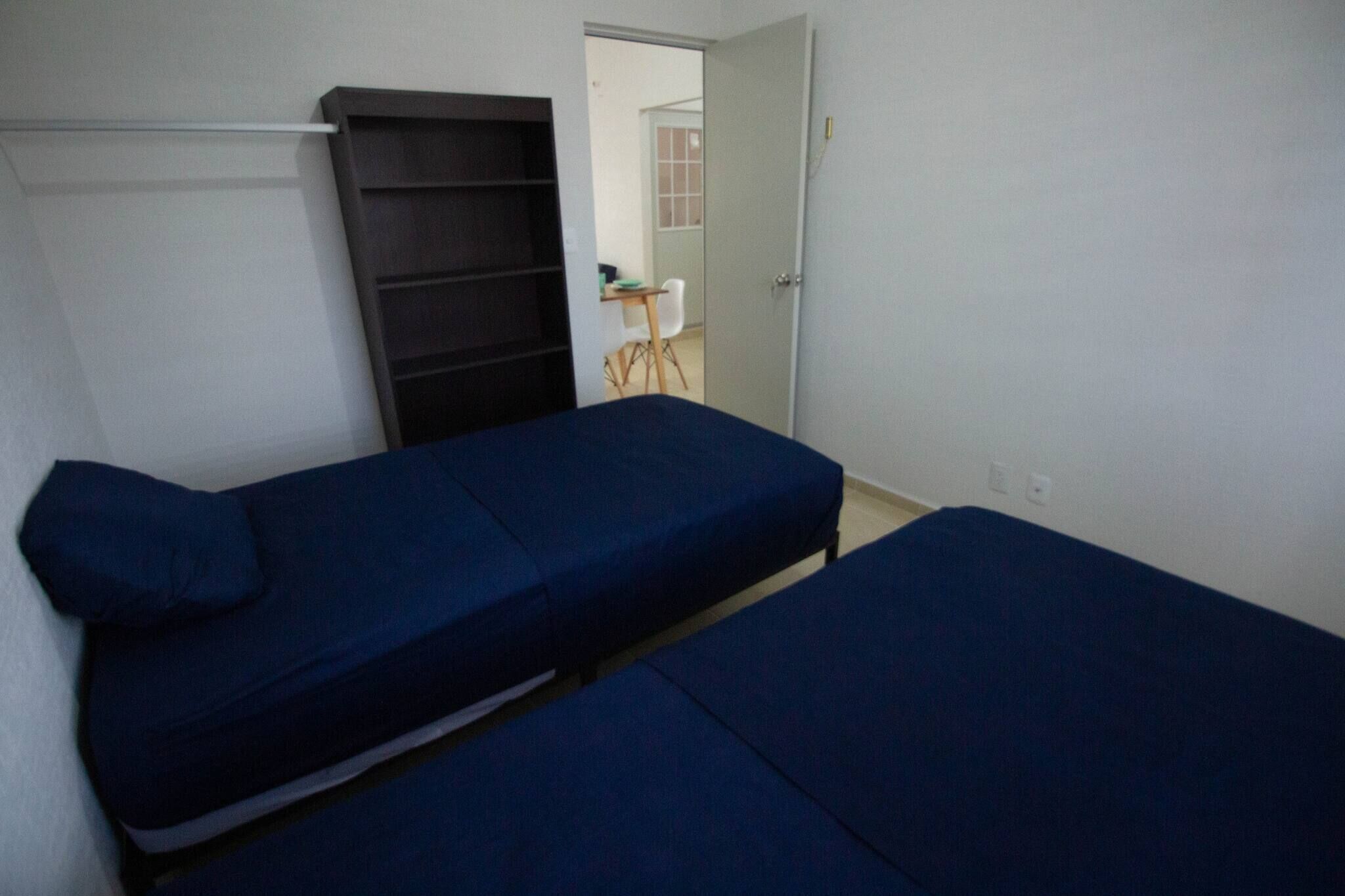 Een kamer met twee eenpersoonsbedden, een garderobe en een bureau met stoel.