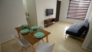 A dining area with a wooden table, white chairs, and a TV on a stand. - Apartment With Pool In Playa Del Carmen (Playa del Carmen)
