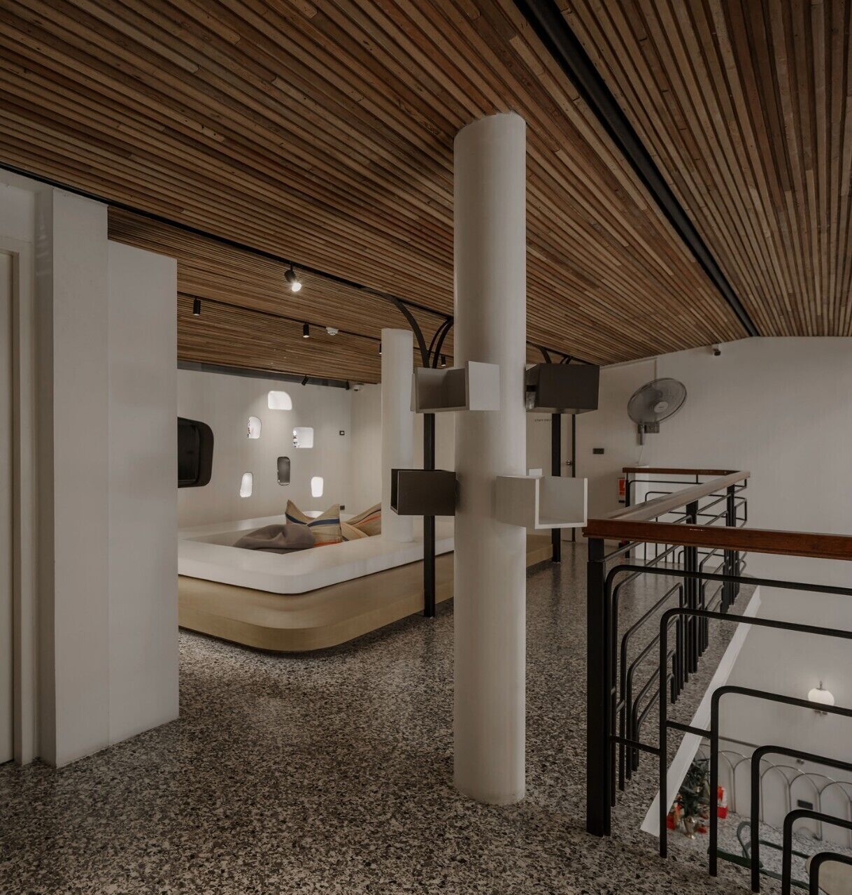 Un intérieur moderne avec un plafond en bois, une colonne centrale et un espace détente agrémenté de coussins.