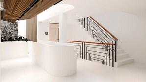 En modern interiör med en vit receptionsdisk, ett tak med träribbor och en trappa med ett geometriskt utformat räcke.