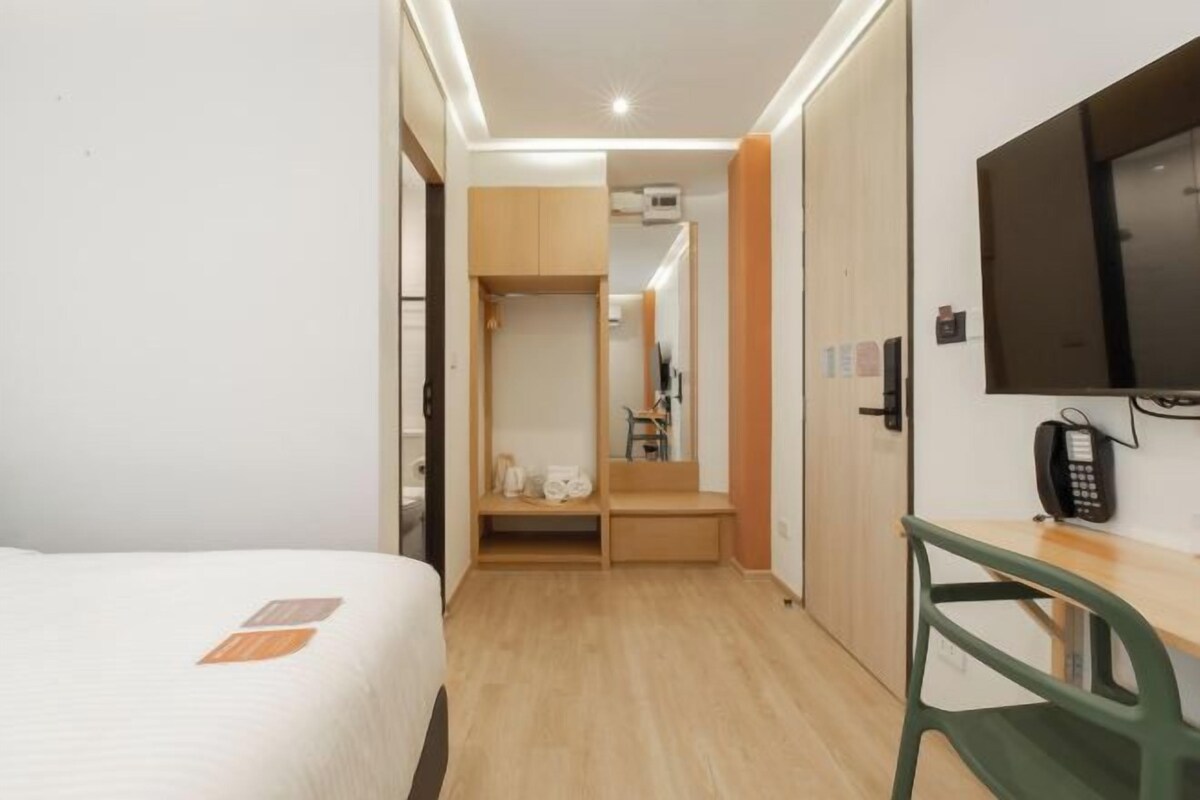 A hotel room with a bed, a desk with a chair, a TV, and a wardrobe.