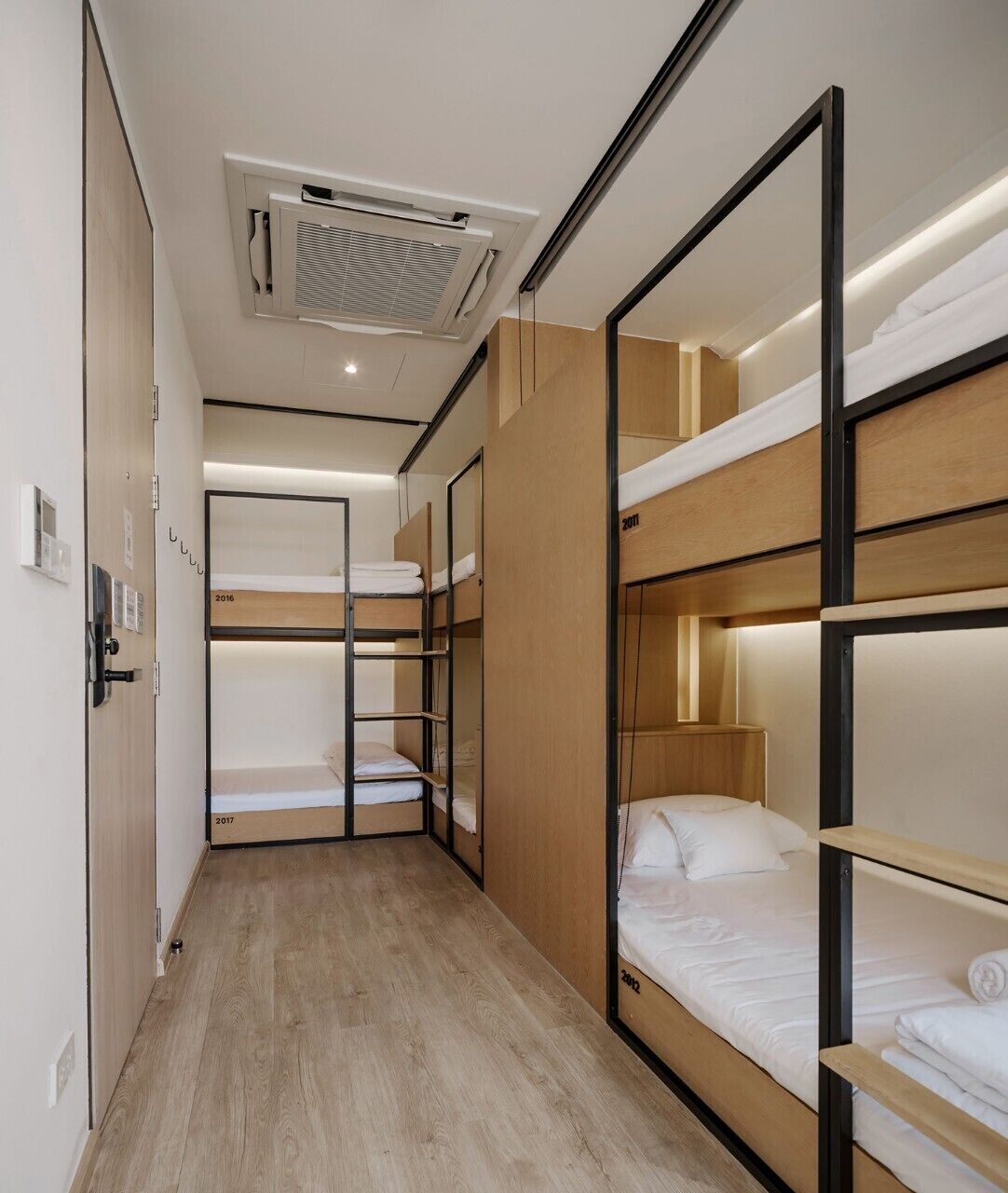 A modern hotel room with bunk beds, wooden flooring, and a built-in wardrobe.