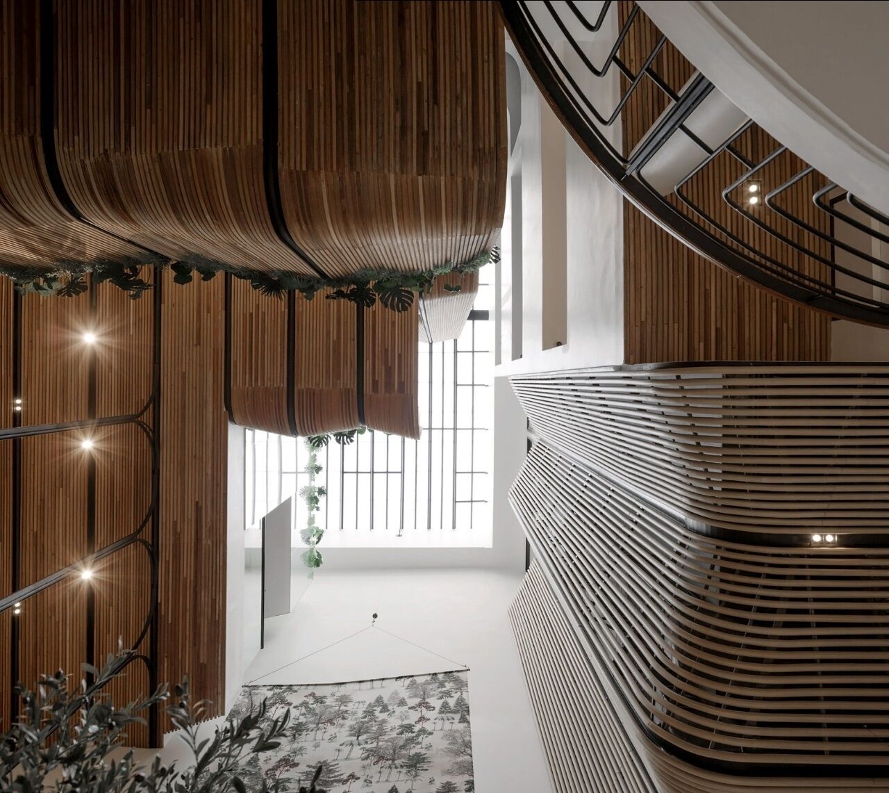 A modern interior with a curved wooden staircase, a ceiling with linear patterns, and a large window with blinds.