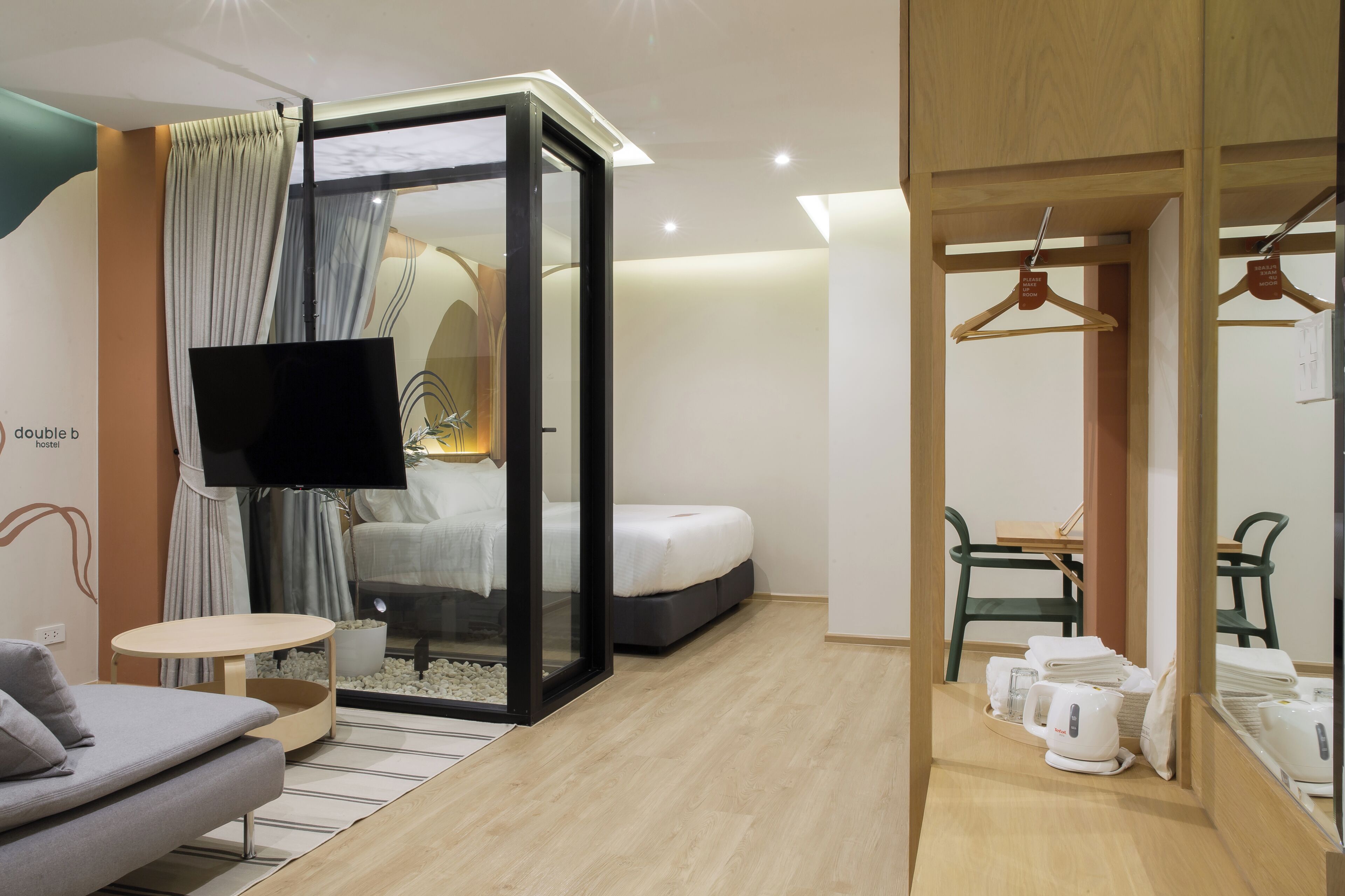 A modern hotel room with a bed, a TV, a seating area with a sofa and a small table, and a kitchenette with a coffee maker.