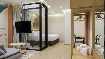 A modern hotel room with a bed, a TV, a seating area with a sofa and a small table, and a kitchenette with a coffee maker.