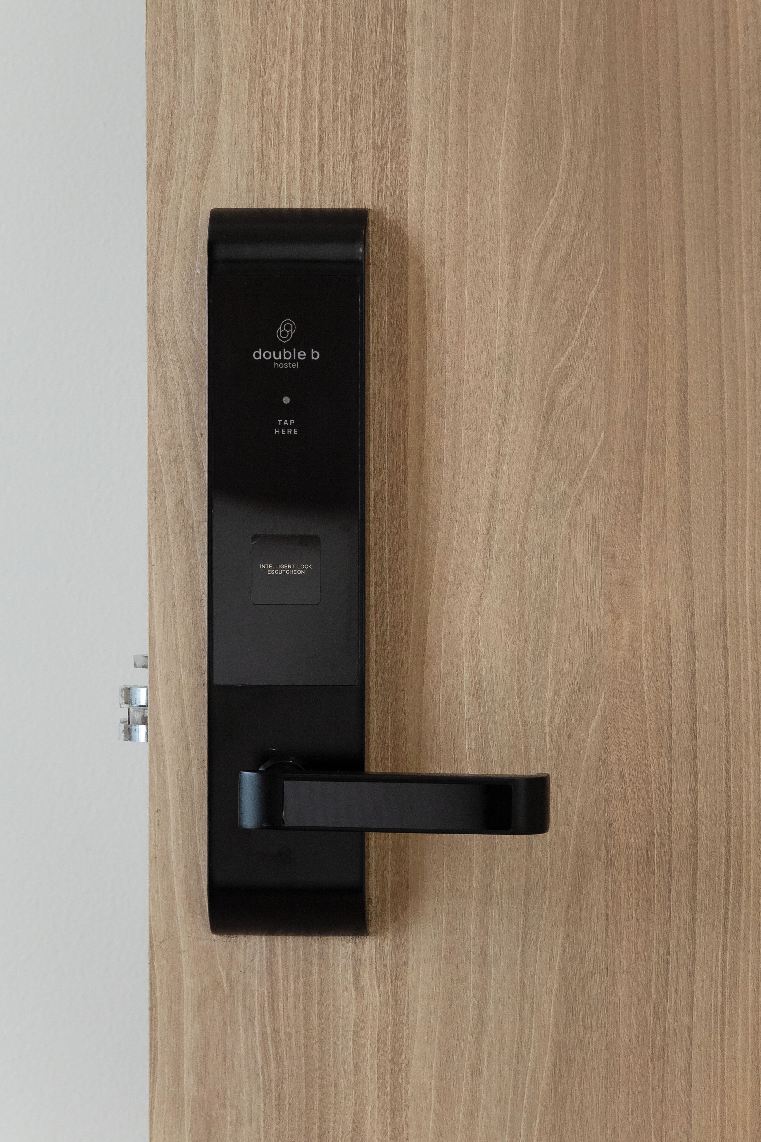 A black electronic lock with a brand logo and the text 'TAP HERE' on a wooden door.