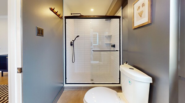 A modern bathroom with a glass-enclosed shower, a white toilet, and a small shelf with toiletries.