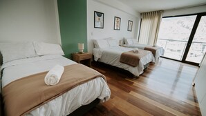 A hotel room with three beds, wooden flooring, and a large window with a view of a snowy landscape. - Spacious 4 Bedroom Full Apartment, a few Minutes From the Main Square (Cusco)