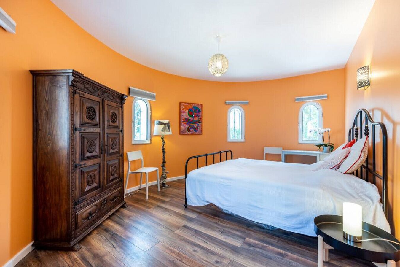 Een slaapkamer met een groot bed, een houten garderobe, een bureau en twee ramen.