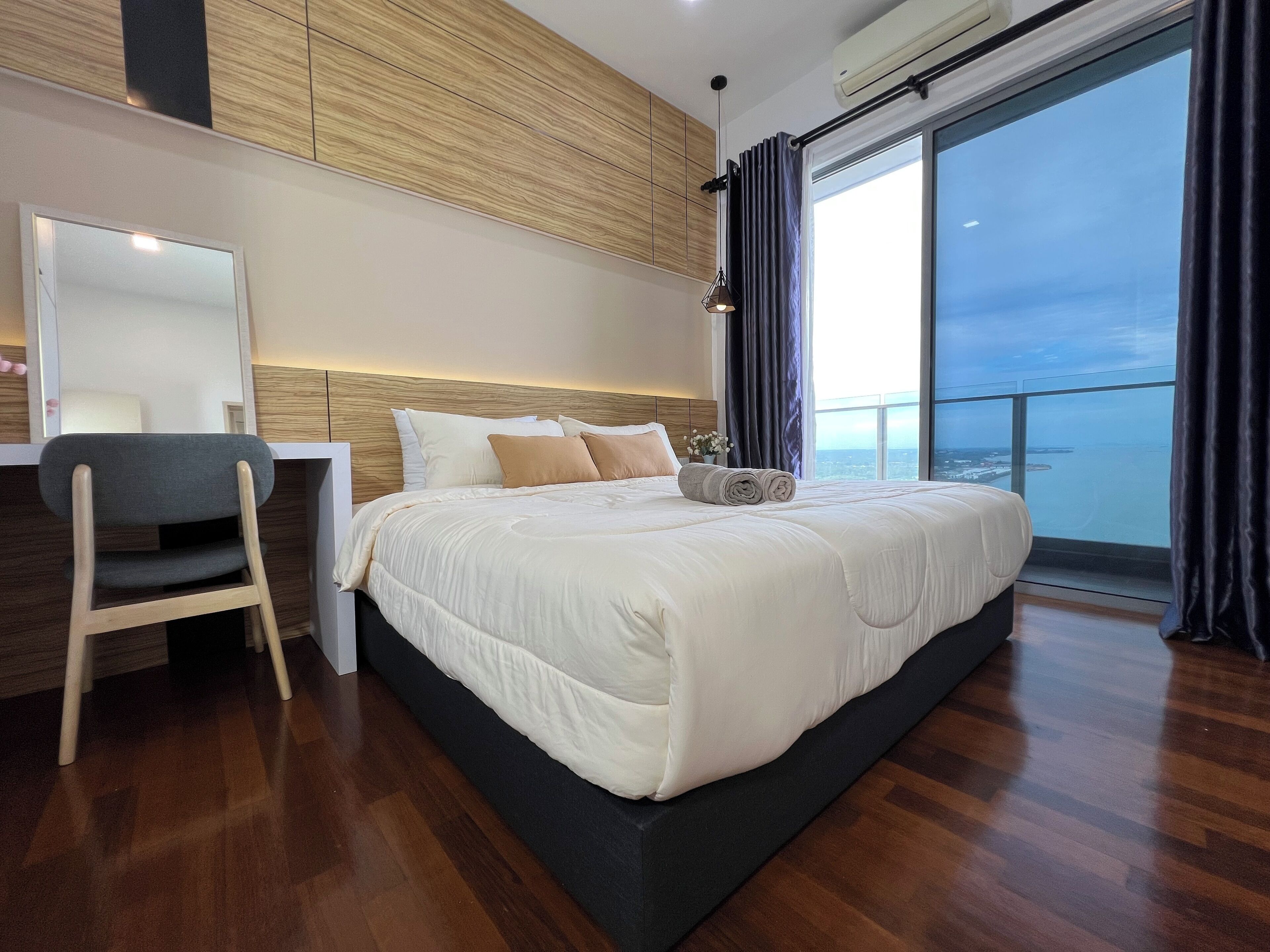 A modern hotel room with a large bed, a desk, and a view of the sea.