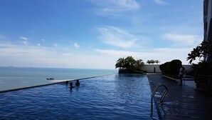 An infinity pool with a view of the sea, palm trees, and a building. - Attic Home Melaka Silverscape Residence (Malacca City)
