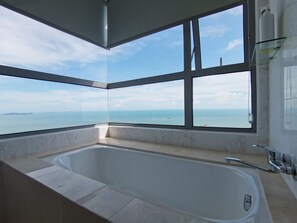 Un baño moderno con una bañera grande, un cerramiento de ducha de vidrio y vistas al mar a través de amplias ventanas.