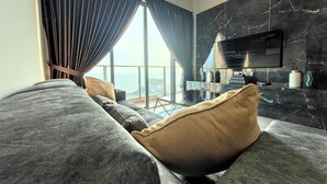 A modern living room with a grey sofa, a TV mounted on a black marble wall, and a large window with curtains. - Attic Home Melaka Silverscape Residence (Malacca City)