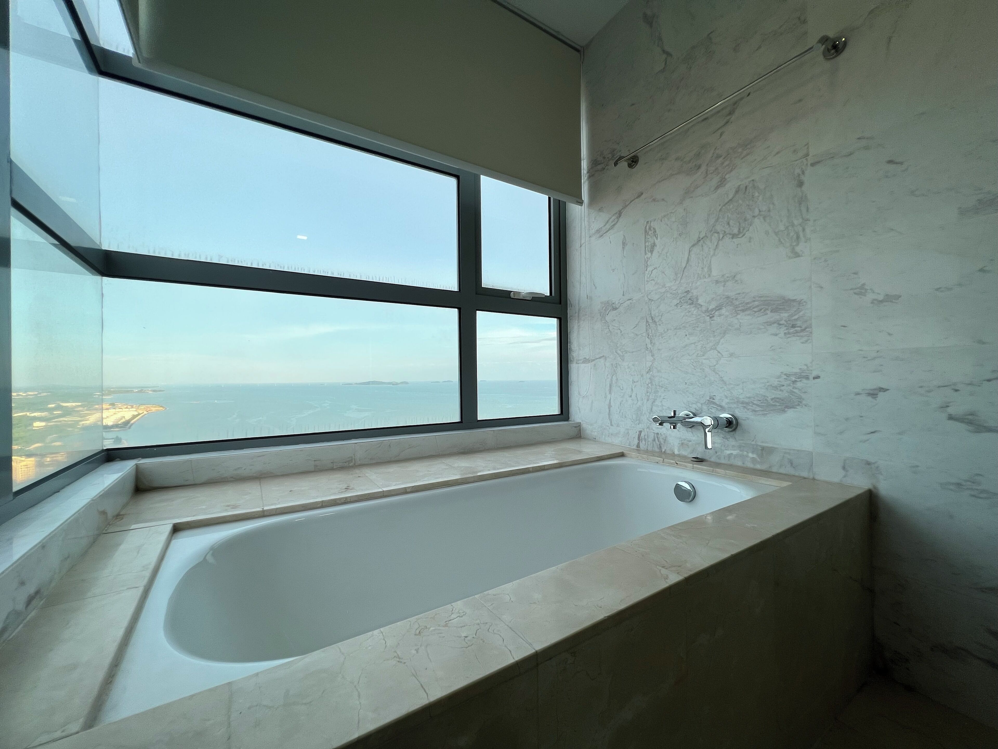 A modern bathroom with a large bathtub, a window offering a view of the sea, and marble walls.
