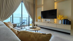 A modern living room with a large sofa, a round coffee table, and a flat-screen TV mounted on a wooden wall. - Attic Home Melaka Silverscape Residence (Malacca City)