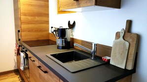 Een moderne keuken met een roestvrijstalen spoelbak, houten kastjes, een koffiezetapparaat en een snijplank.