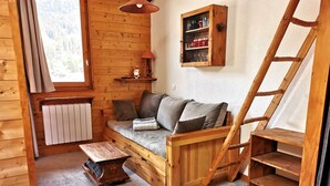 Een gezellig houten chalet van binnen, met een bank, een kleine tafel, een kast en een ladder.