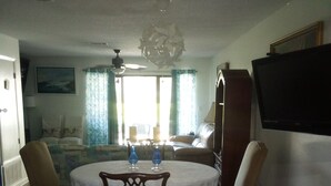 A kitchen with a blue countertop, a dining table with chairs, a TV mounted on the wall, and a fruit bowl on the counter. - Townhouse style condo in beautiful resort across the street from Gulf of Mexico! (Panama City)