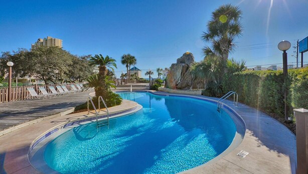 A swimming pool with clear blue water, surrounded by palm trees and a rocky landscape. - Townhouse style condo in beautiful resort across the street from Gulf of Mexico! (Panama City)