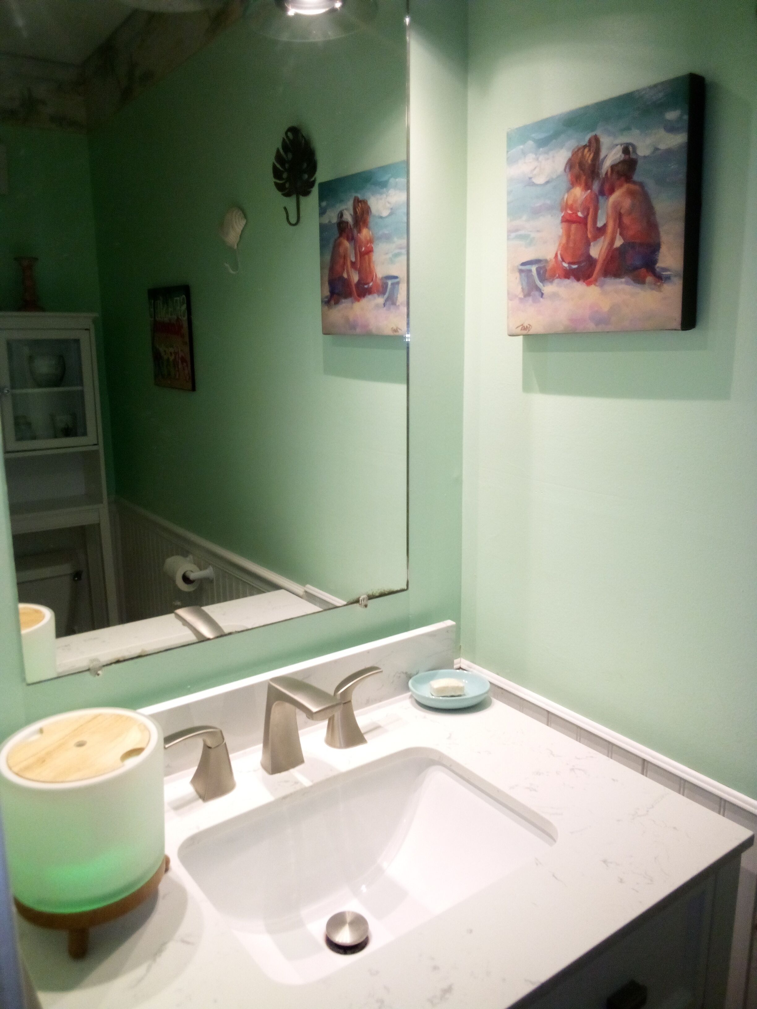 Une salle de bain avec un lavabo blanc, un miroir et deux tableaux accrochés au mur.