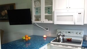 A kitchen with white cabinets, a blue countertop, a microwave, an oven, and a small table with fruit. - Townhouse style condo in beautiful resort across the street from Gulf of Mexico! (Panama City)