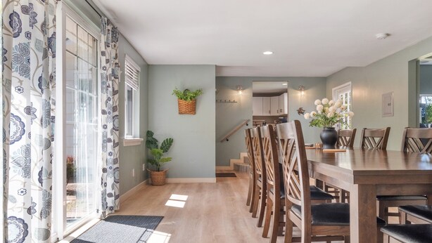 Un coin repas avec une table et des chaises en bois, une plante en pot et un escalier menant à une autre pièce.