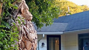 Une sculpture en pierre représentant la tête d’un lion, placée devant une maison dont le toit est foncé et la façade de couleur claire.