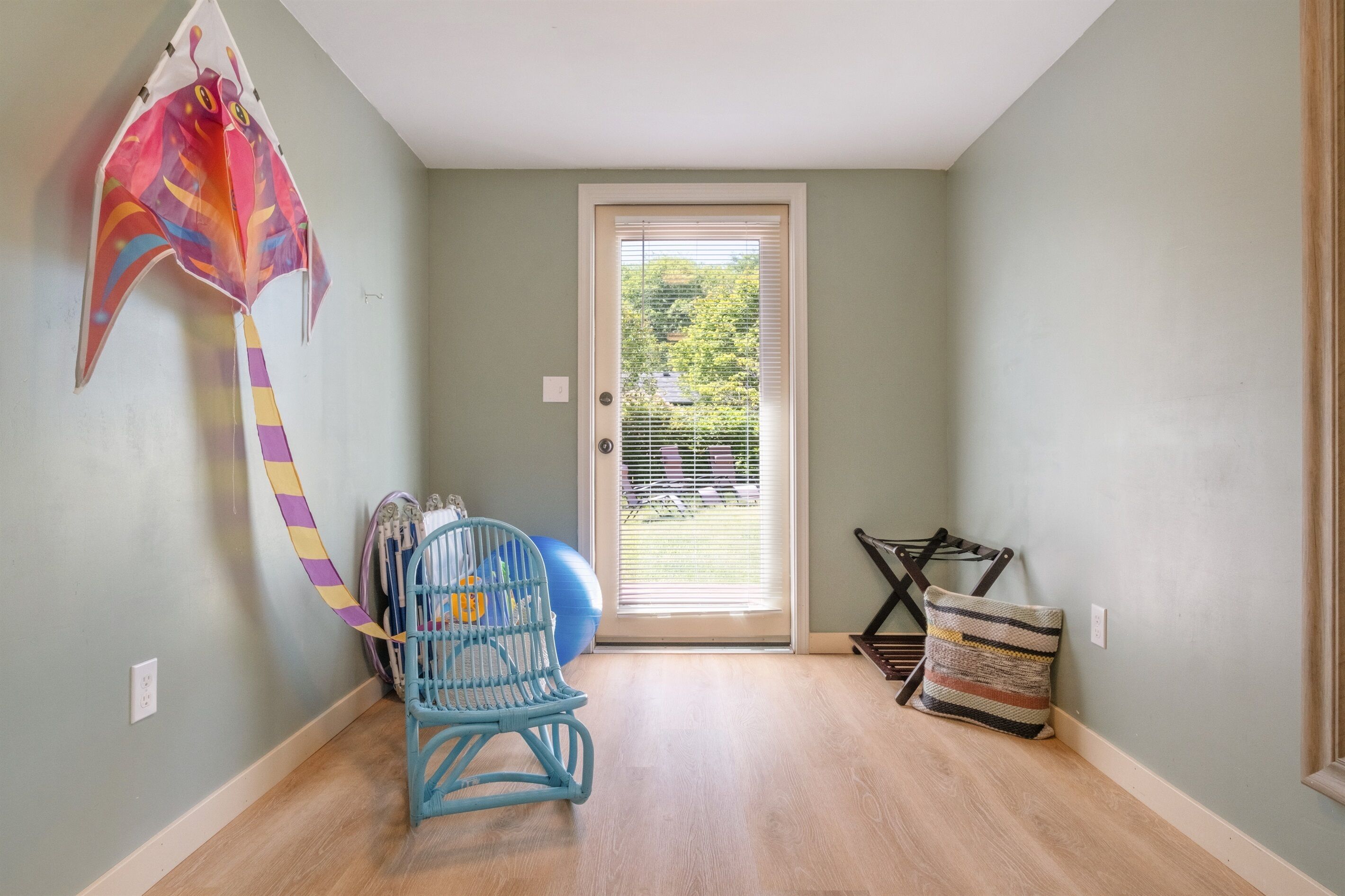 Una habitación con puerta que da a un balcón, una silla azul, una cometa colorida y un cojín estampado.
