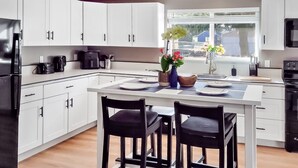 Une cuisine moderne avec des meubles blancs, un réfrigérateur noir, une cuisinière noire et une fenêtre donnant sur l’extérieur.