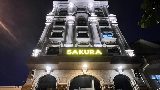 Entrada de hotel con un llamativo letrero 'SAKURA', amplias ventanas en arco y detalles arquitectónicos clásicos.
