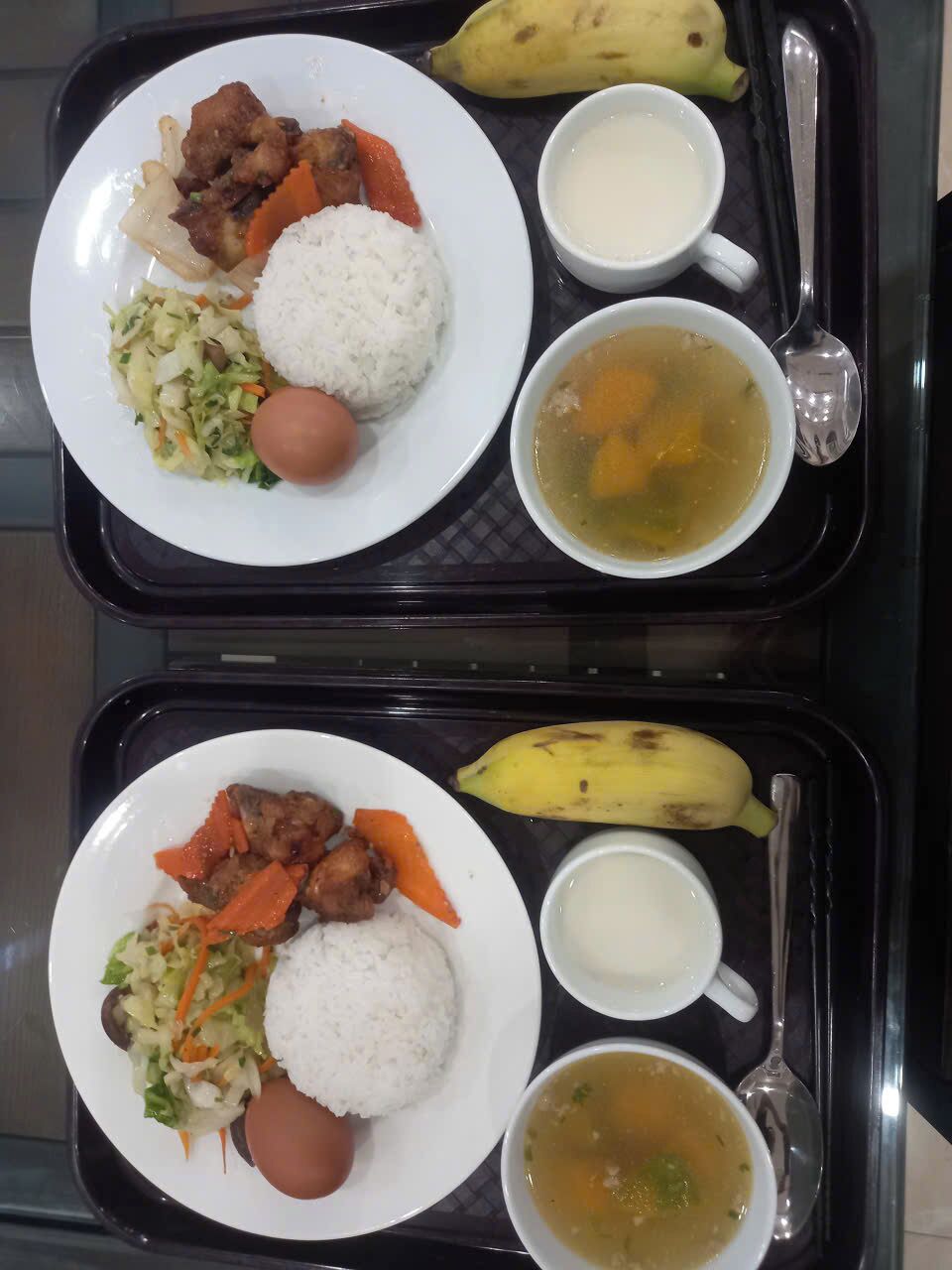 A tray with two plates of food, including rice, meat, vegetables, and a banana.