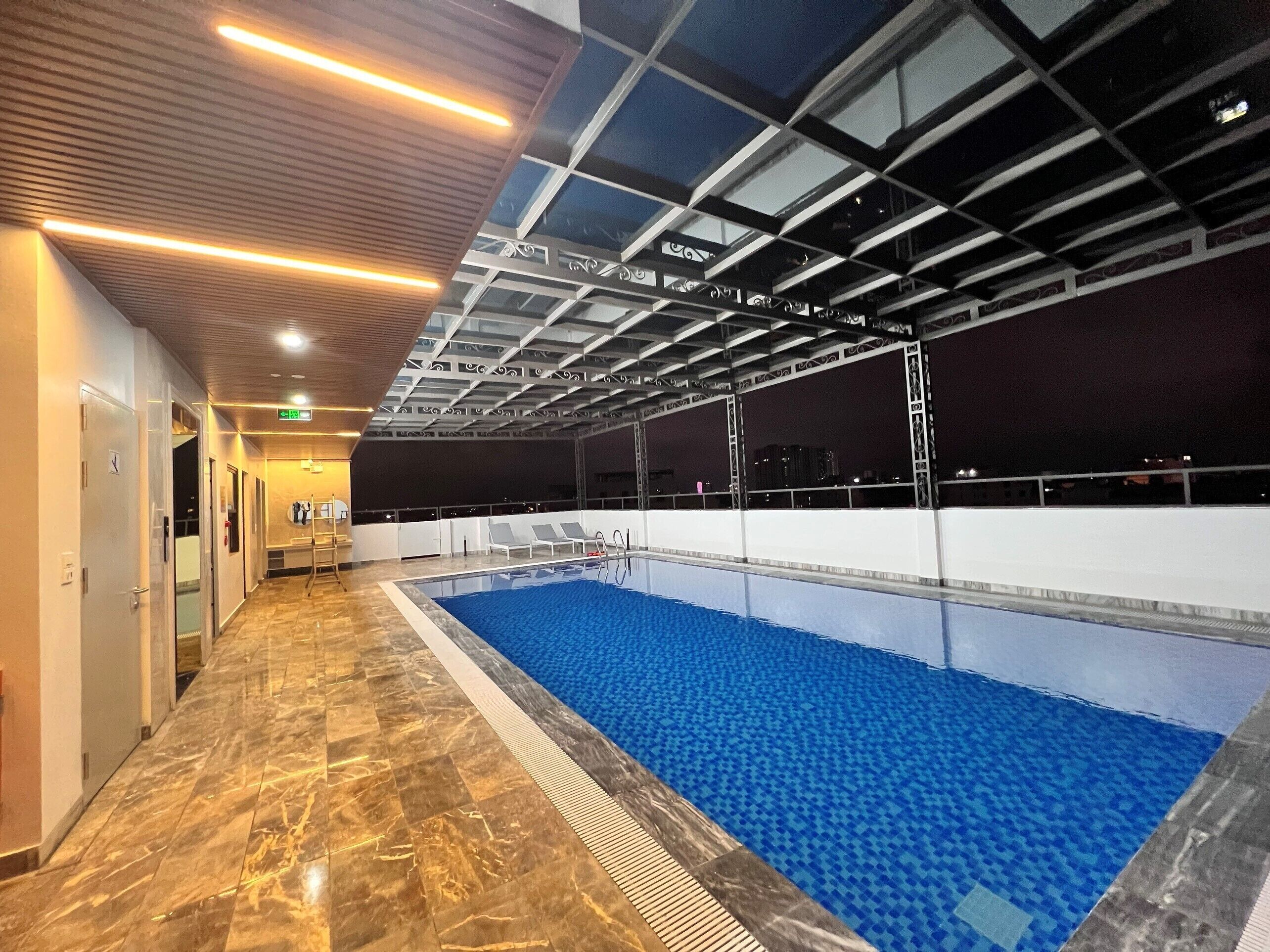 An indoor swimming pool with a clear water surface, surrounded by a tiled floor and a ceiling with a geometric pattern.