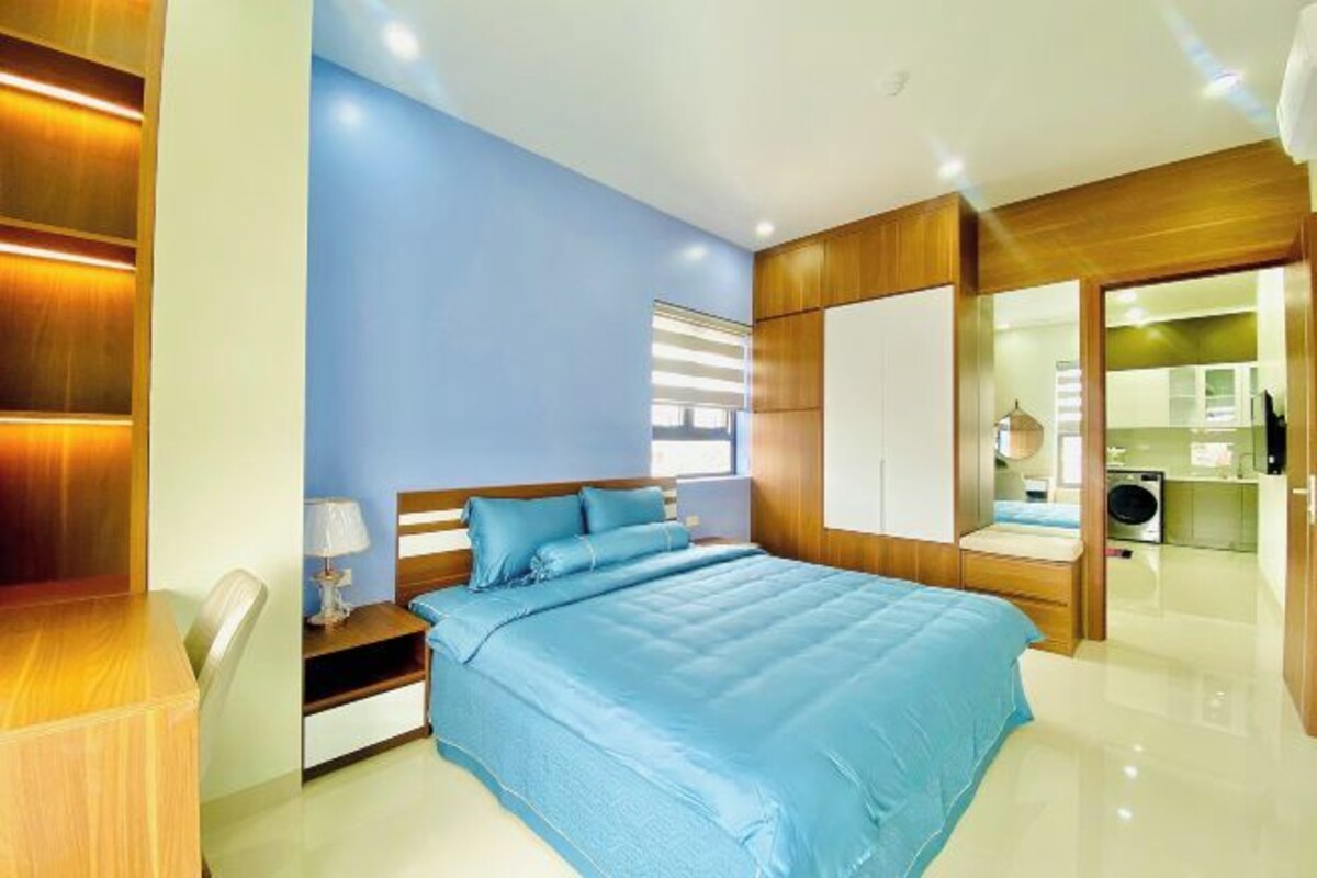 A modern bedroom with a large bed, wooden wardrobe, and a small desk with a chair.